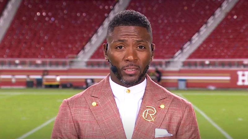 Ryan Clark in a red suit with a football field behind him