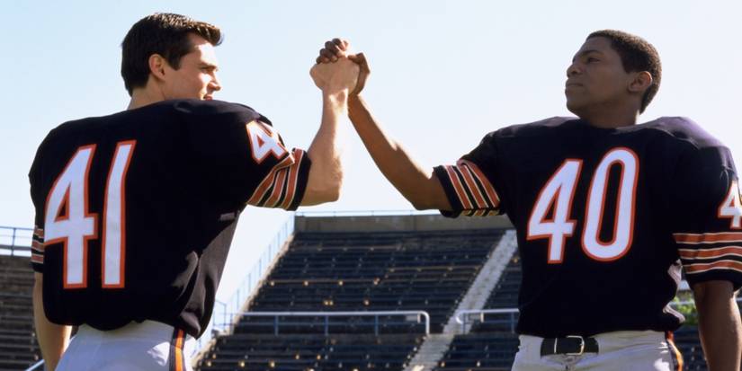 A white football player and a Black football player shake hands