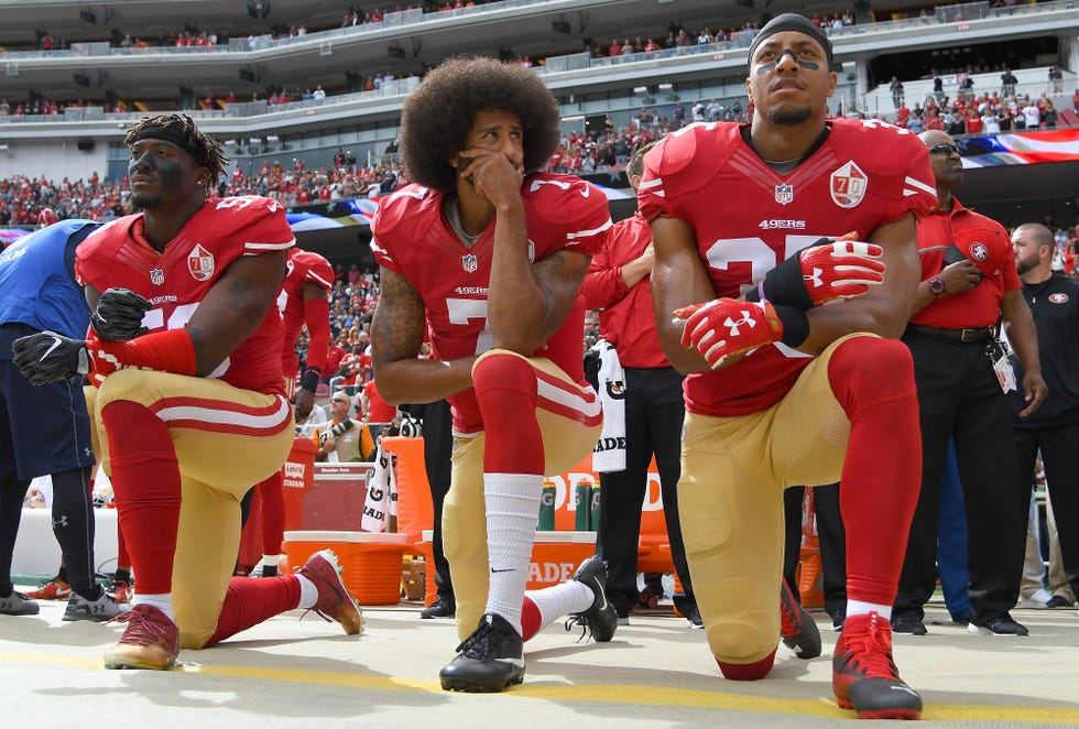 eli harold, colin kaepernick, and eric reid kneel on the sideline at a football game while wearing san francisco 49ers uniforms without helmets