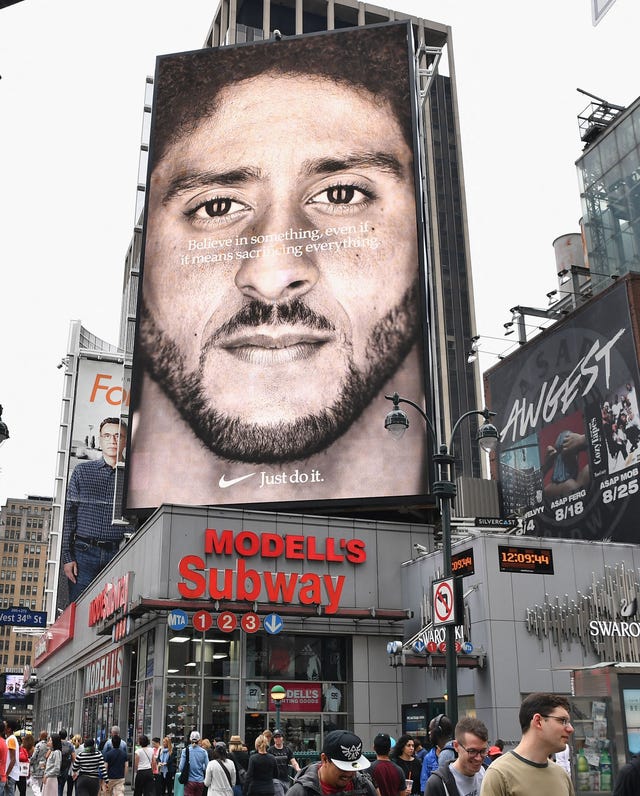 a city corner in new york city featuring a large nike ad with colin kaepernick, above a subway entrance