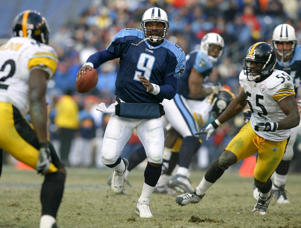 steve mcnair playing in a football game and running between defenders with the ball in his right hand
