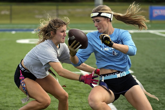 Two women ont he field grapple for the football during a flag football match.