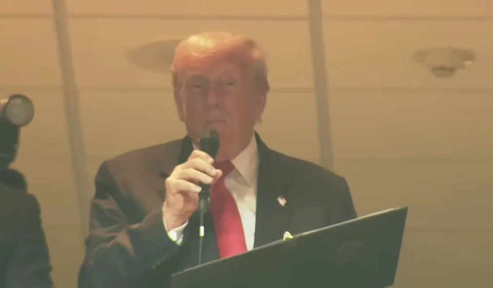 A person in a suit speaks into a microphone at an indoor event location